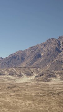 The scene shows a wide desert area with rocky mountains in the background under a blue sky. There are no signs of vegetation or water visible in this dry landscape.