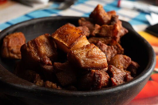 Deep fried pork belly bites served in a rustic black clay bowl close up