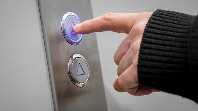 Close up of a hand pressing a glowing elevator button with elevator building transport activation technology interior infrastructure