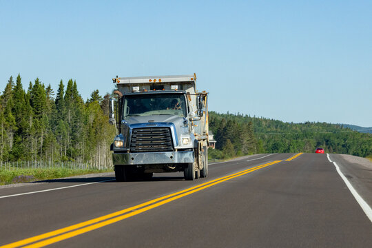 Gaspesie, Quebec, 15 July 2026 : A Freightliner dump truck drives on a rural highway under a clear blue sky.