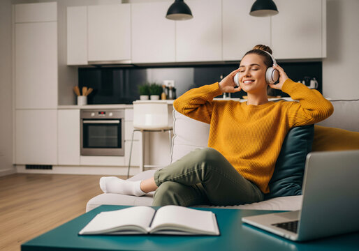 Young fun woman wear casual clothes listen music in headphones drink coffee sits in chair stay at home hotel flat rest relax spend free spare time in living room indoor. People lounge concept.