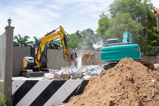 Yellow excavator with hydraulic breaker hammer and green digger breaking reinforced concrete structure at demolition site