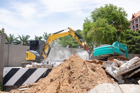 Excavator hydraulic breaker crushing concrete slab with dust cloud rising at demolition site