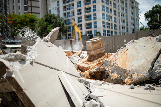 Broken concrete slabs with rebar close-up with excavator using hydraulic breaker in background at demolition site