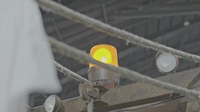 Close-up editorial shot of an amber rotating warning beacon light mounted on an industrial structure with dusty ropes crossing the frame.