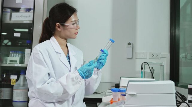 Professional Asian female scientist examining liquid sample in centrifuge tube for eco-friendly biotechnology innovation, sustainable development, and sterile pharmaceutical medical research.