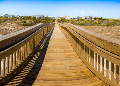 Wooden boardwalk leading to beach homes under a clear blue sky