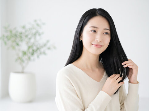 サイドから見つめて毛先を整えるツヤやかな黒髪の女性