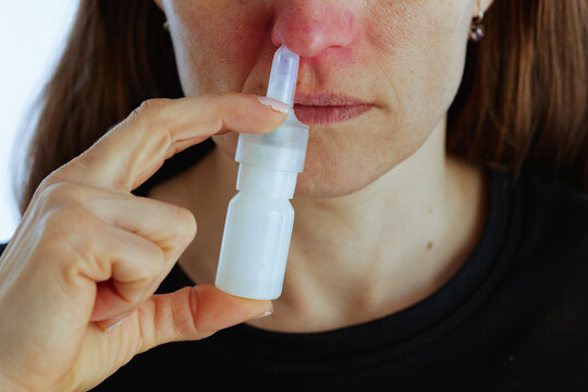 A mid-adult woman applies a nasal spray to treat a blocked nose and irritated skin, demonstrating self-care and home treatment for cold and allergy symptoms.