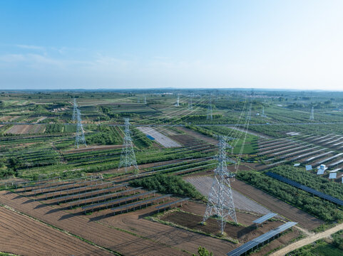 Agricultural fields integrated with photovoltaic power stations and clusters of high voltage transmission towers under clear blue sky