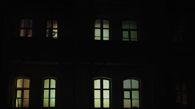 Family Silhouettes Visible Through House Windows at Night
