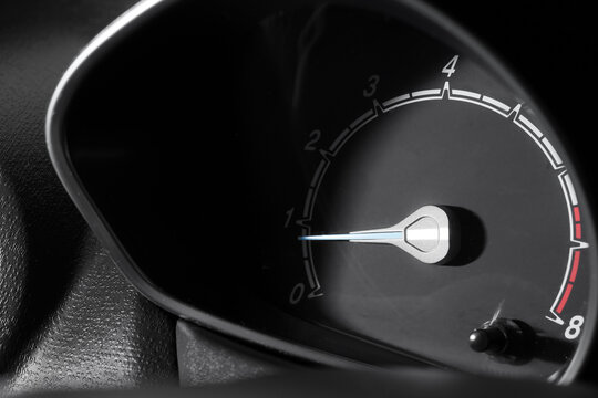 Car dashboard tachometer with glowing needle indicating low revolutions per minute, automotive technology and vehicle performance