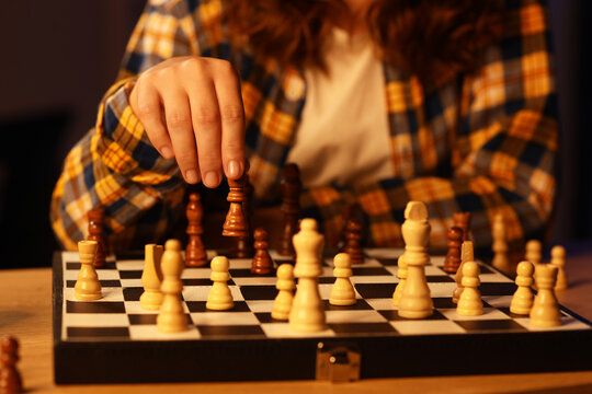 Person in a plaid shirt making a strategic move with a dark chess piece on a chessboard during a game