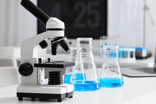 Modern laboratory microscope with blue liquid in conical flasks on a white table scientific research and education