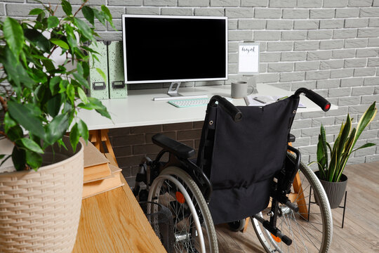 Empty wheelchair at a modern home office desk with a computer monitor and green plants, accessibility and inclusive workspace