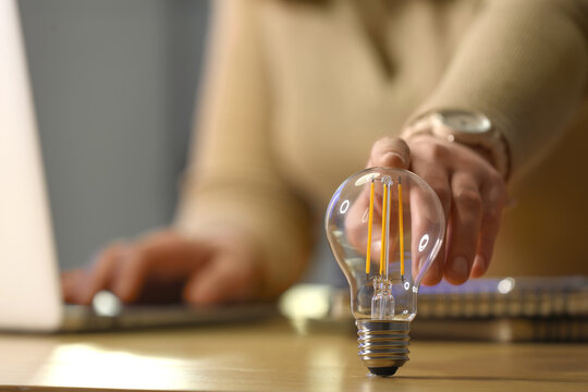 Person reaching for an led light bulb on a wooden desk, innovation and sustainable energy solutions