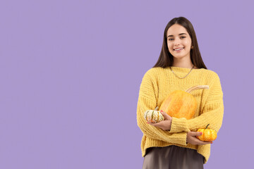 Fototapeta premium Beautiful young happy woman with pumpkins on purple background
