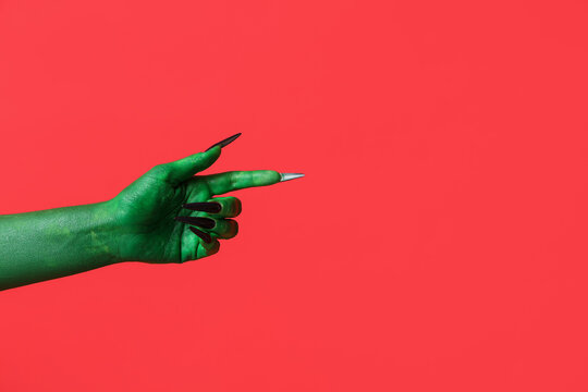 Green hand of witch pointing at something on red background. Halloween celebration