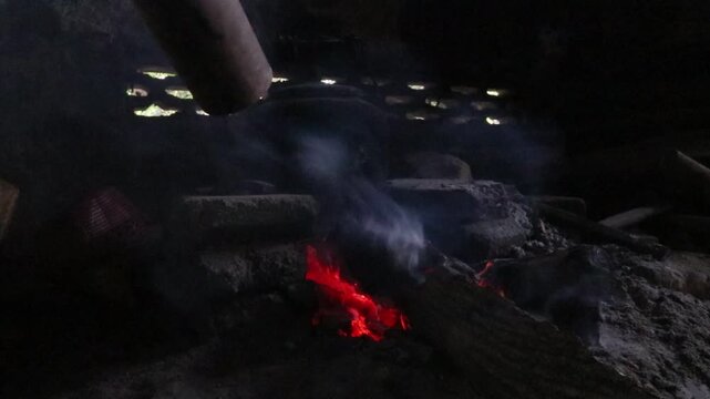Traditional rural kitchen in Java where a wood fire is blown through a bamboo pipe to intensify the flames while boiling water on a simple wood-burning stove.