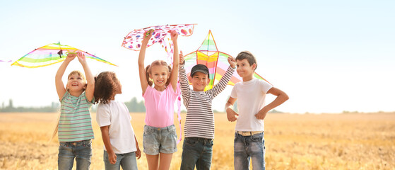 Obraz premium Happy diverse children flying colorful kites in a golden field under a clear sky, enjoying summer outdoor activities