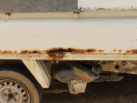 Severe rust damage and corrosion holes on the side frame of an old truck body