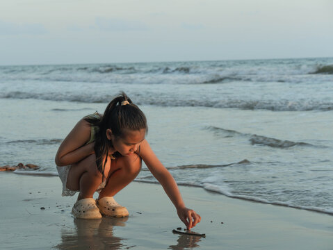 Asian girl crouching down drawing and writing on wet sand at beach shore with ocean waves background