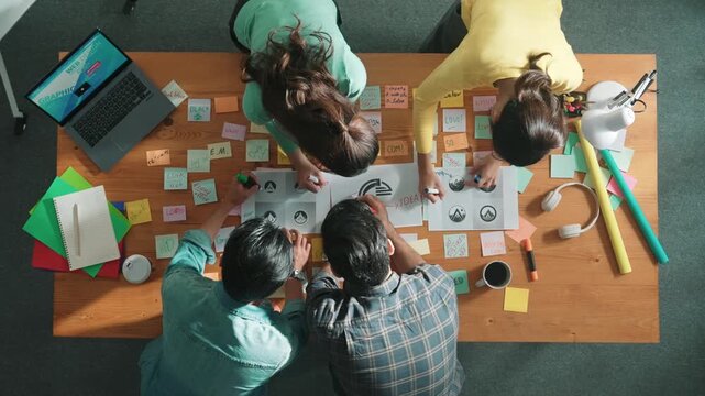 Time lapse of business team put graphic logo on meeting table with colorful sticky notes and start to design while explain idea. Project manager walking at group while explain concept art. Symposium.