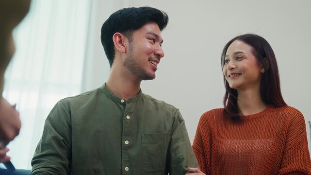 Asian female financial advisor discuss showing tablet to young couple on sofa in living room at home. Insurance consultation plan, house estate mortgage loan meeting, corporate banking broker concept.