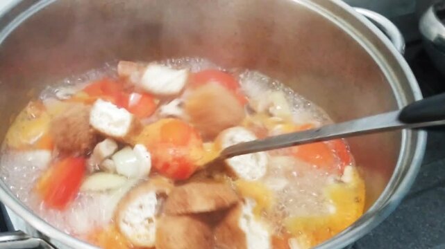 close up kitchen activity, cooking  tomato soup in a hot boiling water, there is a steam coming up. Homemade food preparation.