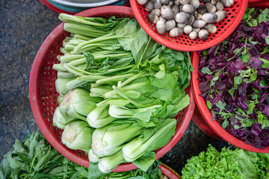 Baskets filled with fresh healthy pak choy salad and basil leaves selling at street food market, exotic food ingredients on sale, vendors offering various assortment of organic vegetables and greens.