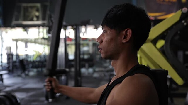 Asian man exercising chest on a press machine in the gym. Athlete doing strength training workout in a gym.