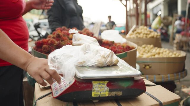 Vendor Weighing Langsat Fruit and Handing Order to Customer at Local Market