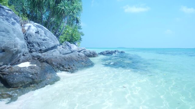 Slow motion: waves on rocky tropical shoreline with crystal clear turquoise sea in Karimunjawa National Park Indonesia lush vegetation and tranquil island scenery
