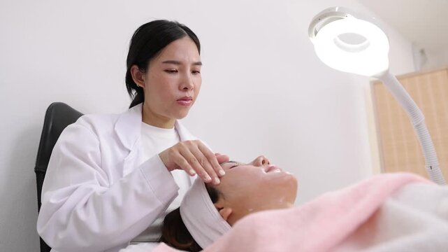 Esthetician applying facial mask and massaging woman's face. Professional cosmetologist giving a facial treatment to a client. Beautician applying skincare cream and massaging the face in a spa.