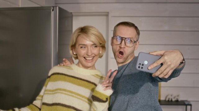 Caucasian couple taking selfie on smartphone while cooking in kitchen. Footage is perfect for promoting culinary apps, modern lifestyle brands, or mobile connectivity campaigns