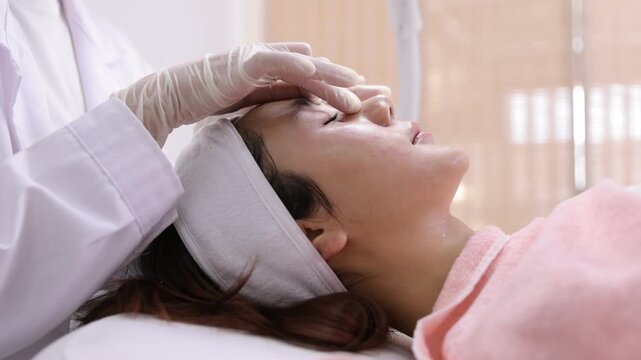 Dermatologist massaging a woman's face during facial treatment. Professional dermatologist massaging a young asian woman's face. Beauty specialist providing skincare treatment in a cosmetic clinic.