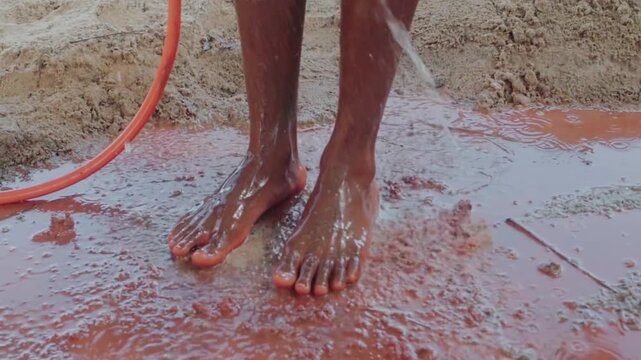 Close up of a native artisan washing their dirty bare feet with a water hose after kneading clay for pottery, an ancestral manual process
