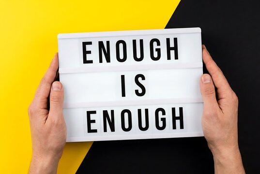 Hands holding a lightbox with "ENOUGH IS ENOUGH" text on a yellow and black background. Motivation and protest concept.