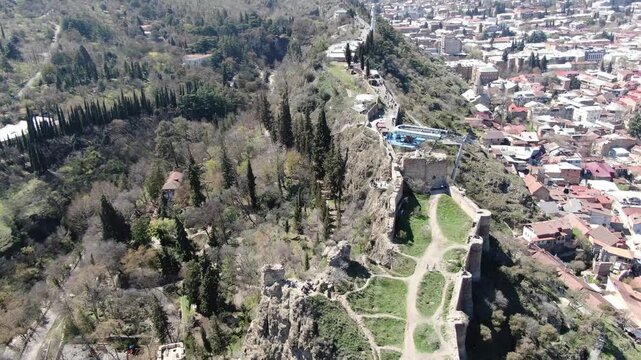 Aerial view of the ancient stone walls and towers of Narikala Fortress overlooking the lush green parklands and historic areas of Tbilisi, Georgia.