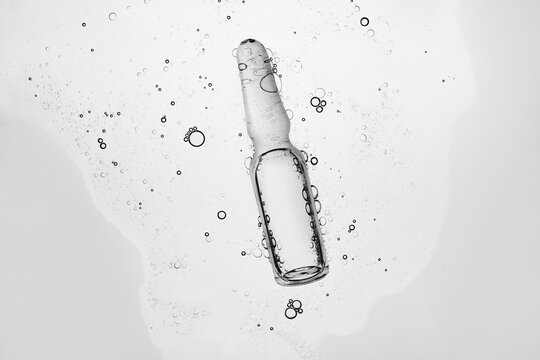 Glass medical ampoule in transparent liquid with air bubbles on gray background