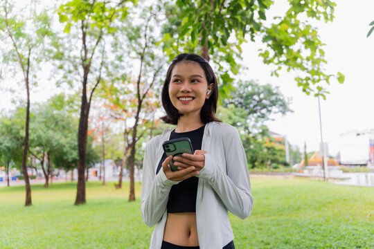 Asian sporty woman using earphone listen to music on smartphone in public park