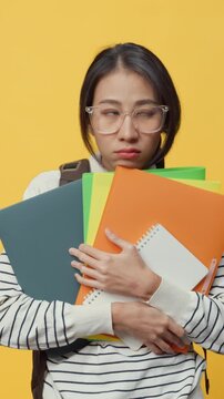 Vertical Screen : Unhappy Asia lady freelance worker casual cloth and backpack holding work file feeling uncomfortable boring and tired with overwork and in copy space isolated on yellow background.