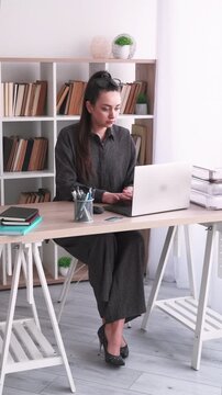 Vertical video. Manager lifestyle. Office atmosphere. Business woman drinking coffee typing laptop using notebook at desk at professional workplace.