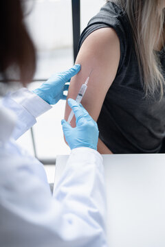 Female doctor administering injection into upper arm of Asian female patient during medical treatment at healthcare clinic.