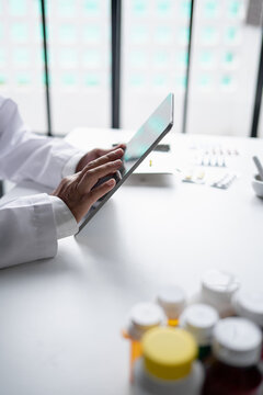 Asian senior female pharmacist using digital tablet representing modern pharmacy pharmaceutical care healthcare technology and medication safety.