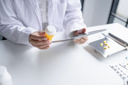 Asian senior female pharmacist using digital tablet representing modern pharmacy pharmaceutical care healthcare technology and medication safety.