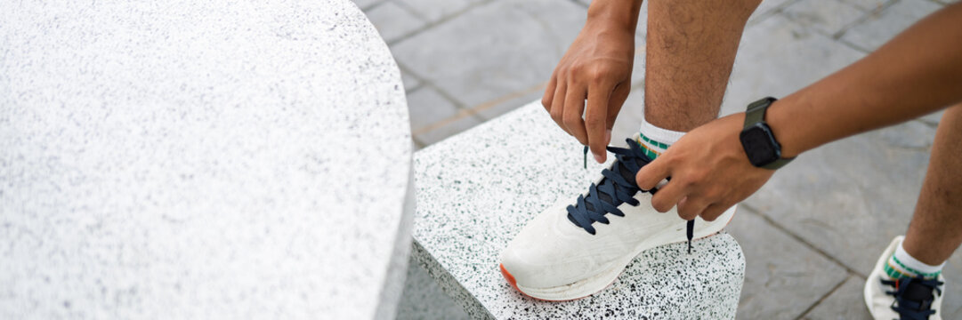 African American mixed race man tying running shoes before workout in urban park.