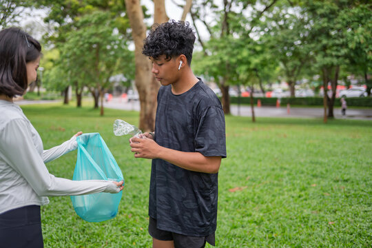 Multicultural Gen Z friends Asian woman and African American mixed race man plogging and collecting trash in green urban park for representing sustainability wellness and positive active lifestyle.