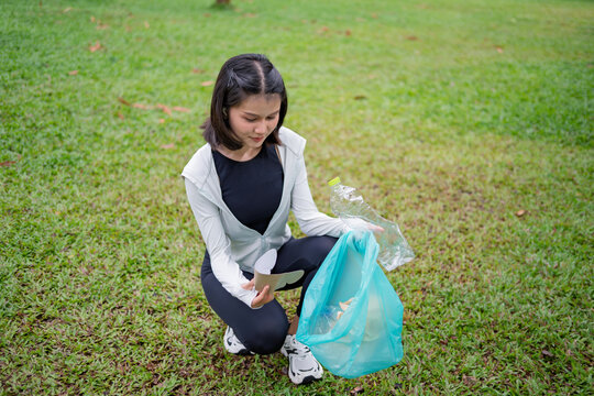 Asian Gen Z woman plogging and collecting trash in green urban park for representing sustainability wellness and positive active lifestyle
