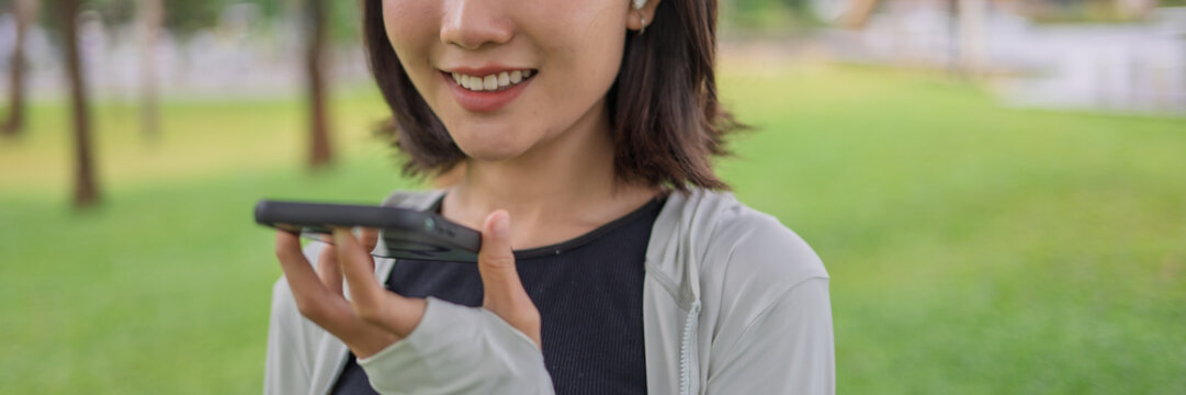 Asian Gen Z woman using AI fitness tracking app on smartphone before jogging in green urban park.